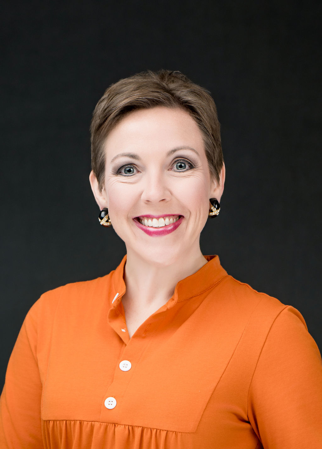 Smiling woman with short hair in an orange blouse, studio headshot